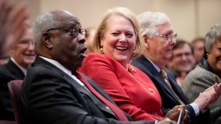 Clarence Thomas and Ginni Thomas laugh while seated in a crowd.