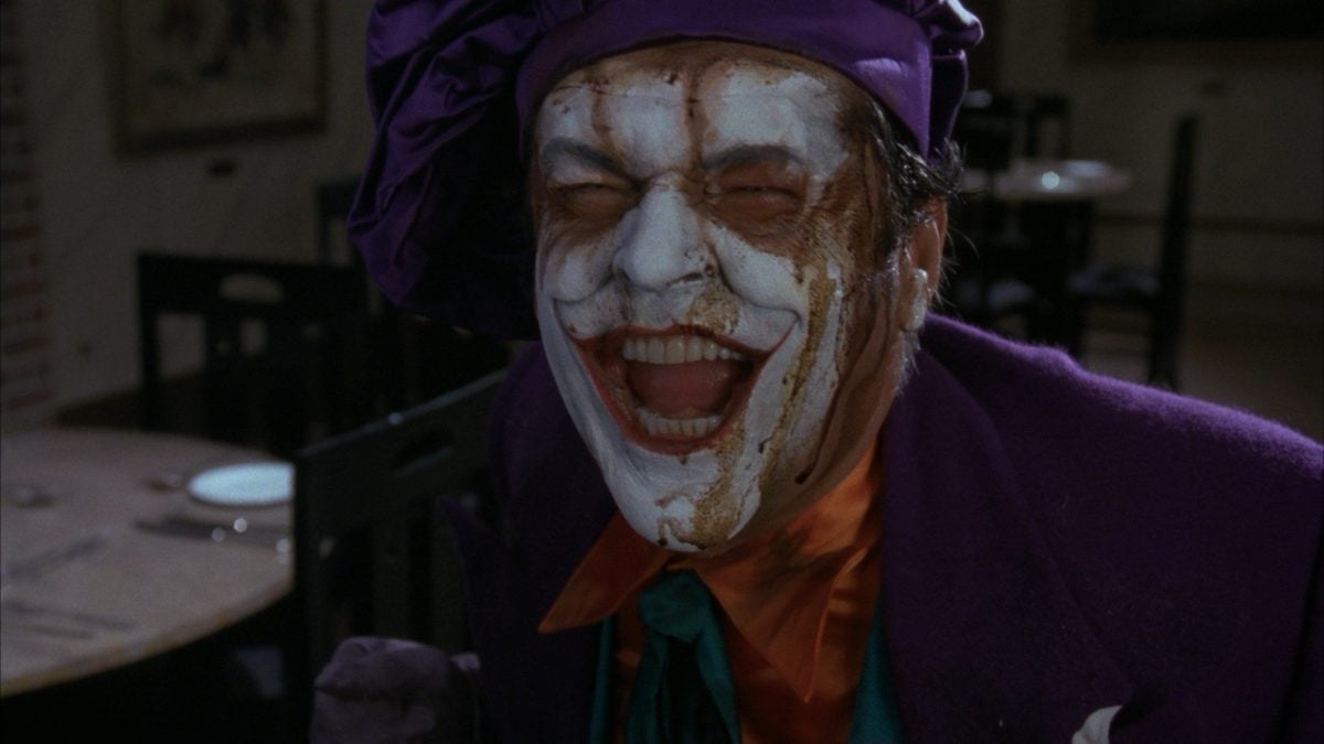 Jack Nicholson laughing as the Joker in Batman (1989). In a purple chef's hat and makeup running down his face. 