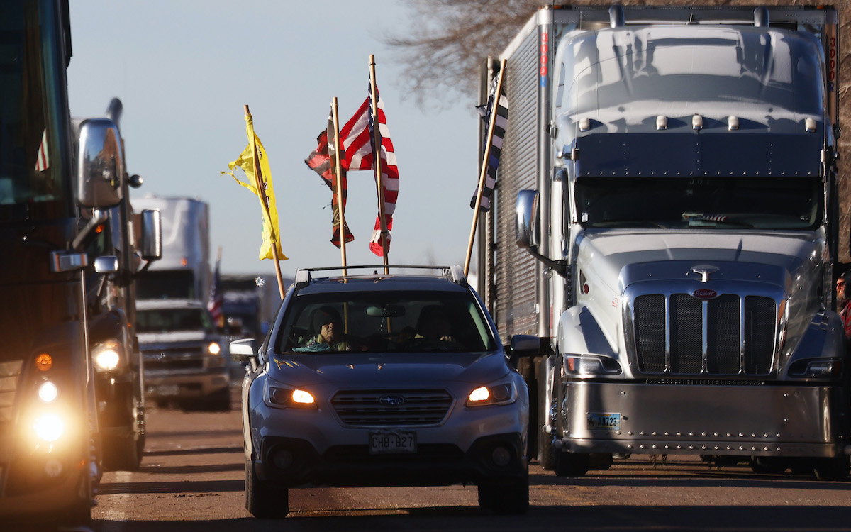 Trucks and cars drive in a convoy, displaying American and "don't tread on me" flags
