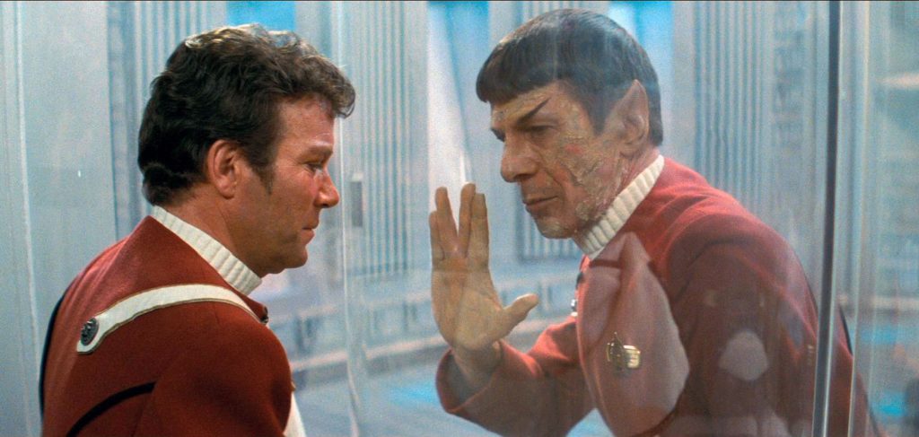 Kirk and Spock separated by glass and Spock gives him the vulcan salute