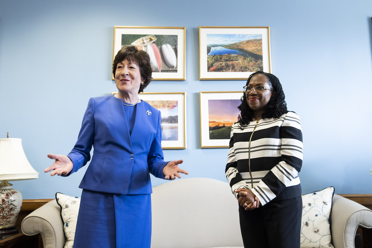 Susan Collins speaks and gestures toward the camera while Ketanji Brown Jackson stands next to her with her hands clasped in Collins' office