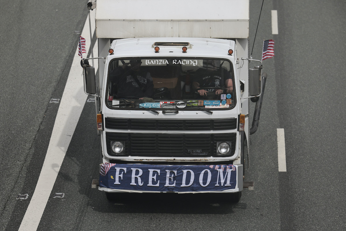 A truck on a freeway with a flag draped across the front reading "freedom"