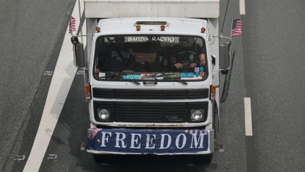 A truck on a freeway with a flag draped across the front reading 