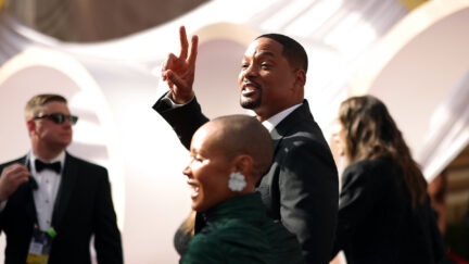 Will Smith flashes a peace sign as he and Jada Pinkett Smith walk the Oscars red carpet
