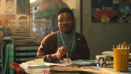 Mr Ajayi, a black 30-something art teacher, sits in his classroom and smiles slightly in a scene from Heartstopper