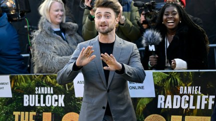 Daniel Radcliffe gestures wildly on the red carpet for The Lost City while people laugh in the background