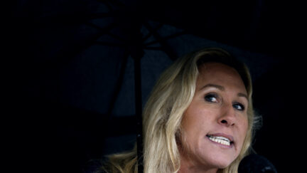 Marjorie Taylor Greene grimaces under a black umbrella.