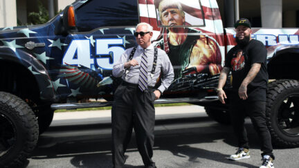 Roger Stone dances next to a rapper in front of a truck decorated with a painting of Donald Trump as Rambo