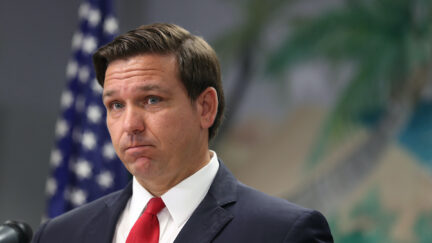 Ron DeSantis looks uncomfortable, stands in front of an American flag