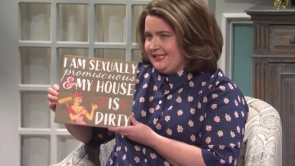 In an SNL sketch, Aidy Bryant holds a wooden sign reading 