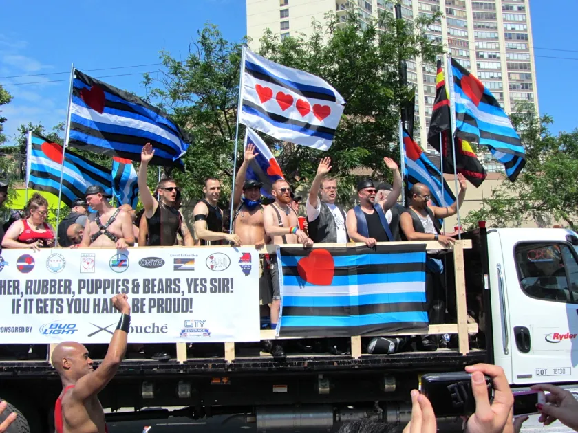 A group of bears and leathermen wave from a Pride truck.