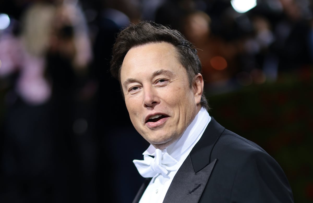 Elon Musk wears a tuxedo with a white bowtie and smiles at the camera with an open mouth