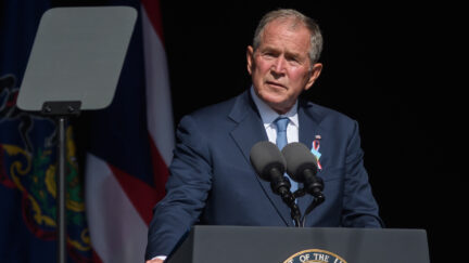 George W. Bush stands at a podium, squinting at a teleprompter