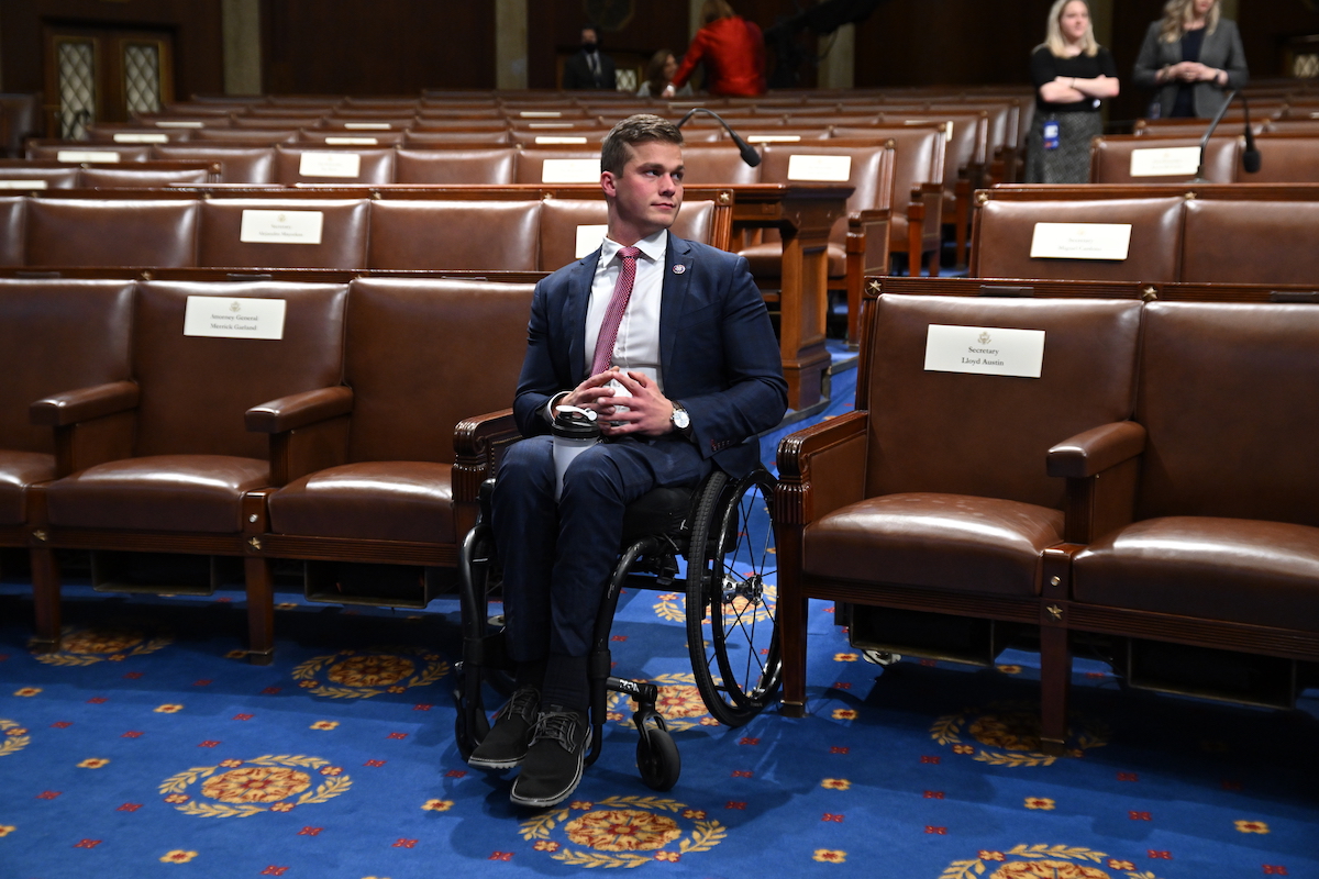 Madison Cawthorn sits in a wheelchair in a Capitol chamber, surrounded by empty seats, looking around for someone to talk to