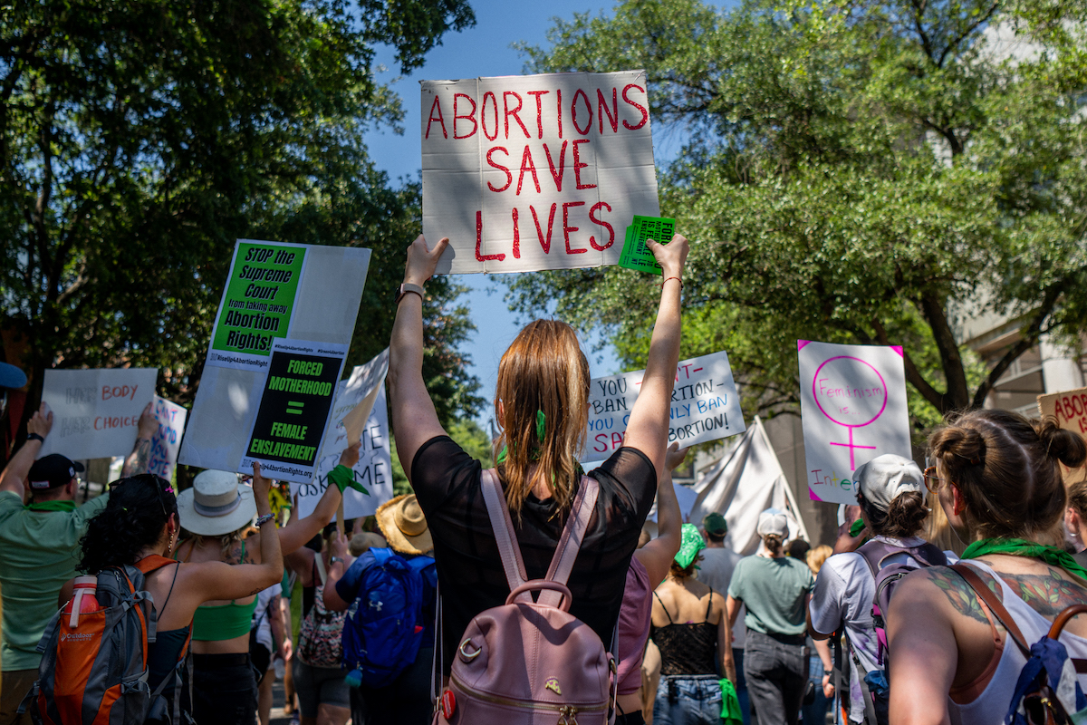 Abortion rights activists and supporters march outdoors, holding signs.