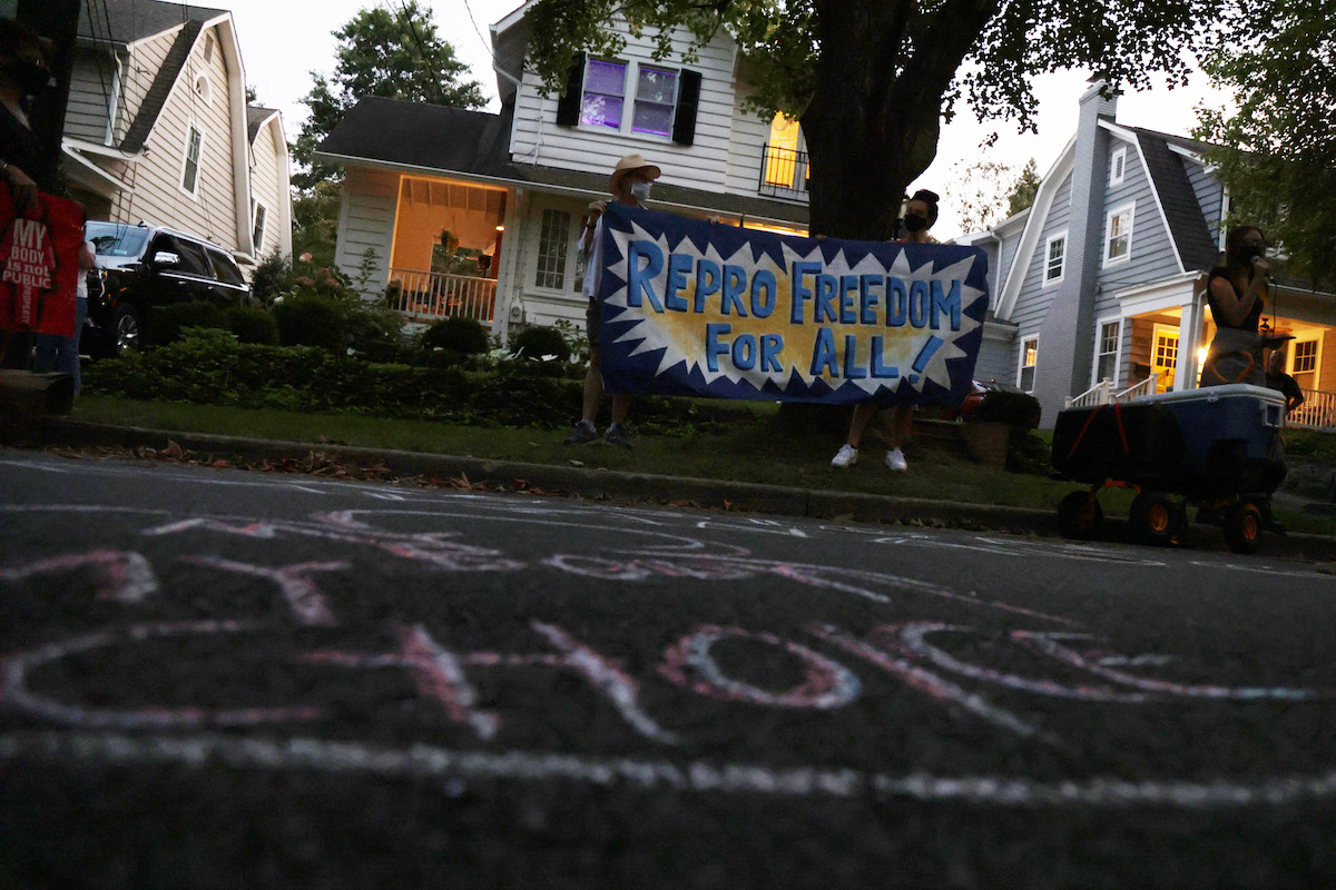 A small group of protesters gather in a residential neighborhood with a banner reading "repro freedom for all"