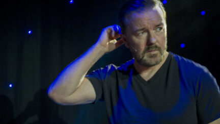 Ricky Gervais scratches his head and looks concerned during a standup comedy special.
