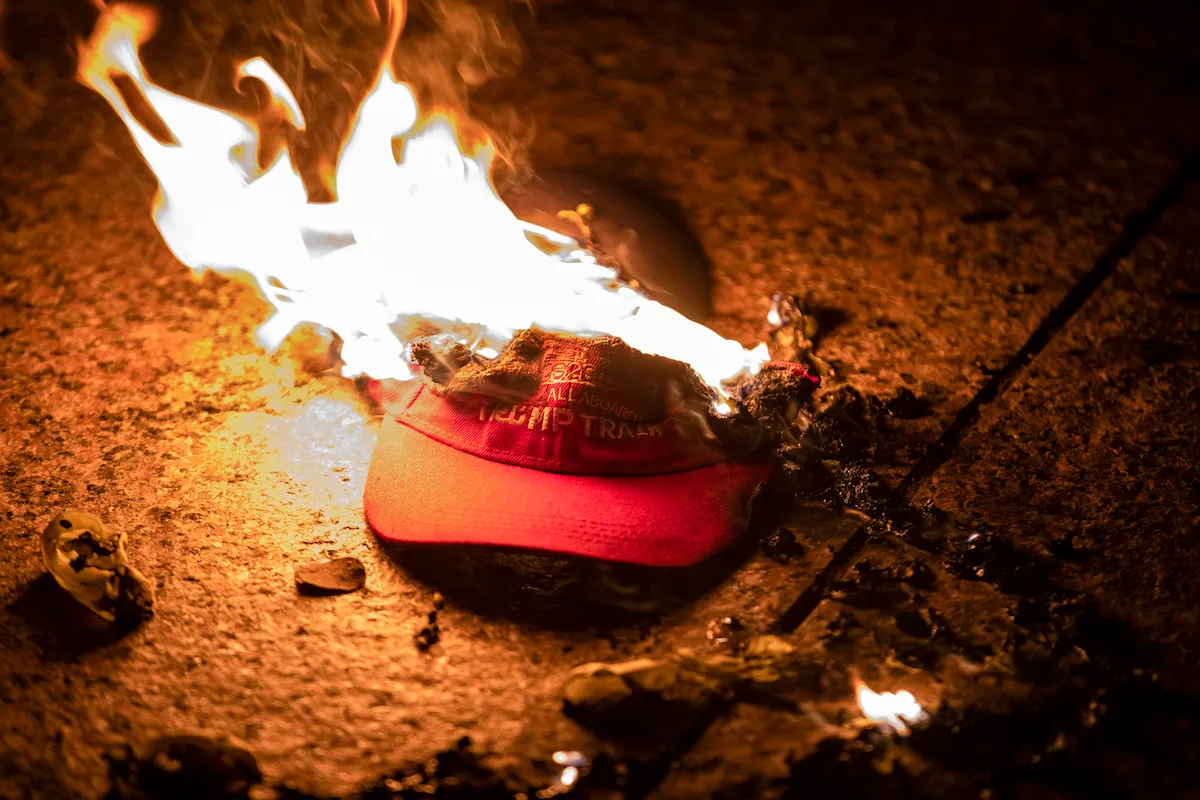 A red MAGA "Trump Train" hat sits on the ground on fire