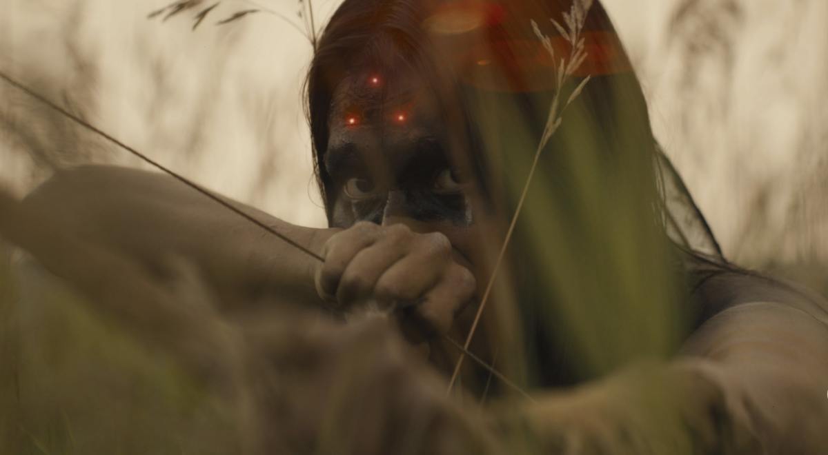 Taabe drawing his bow, with three red target dots on his forehead