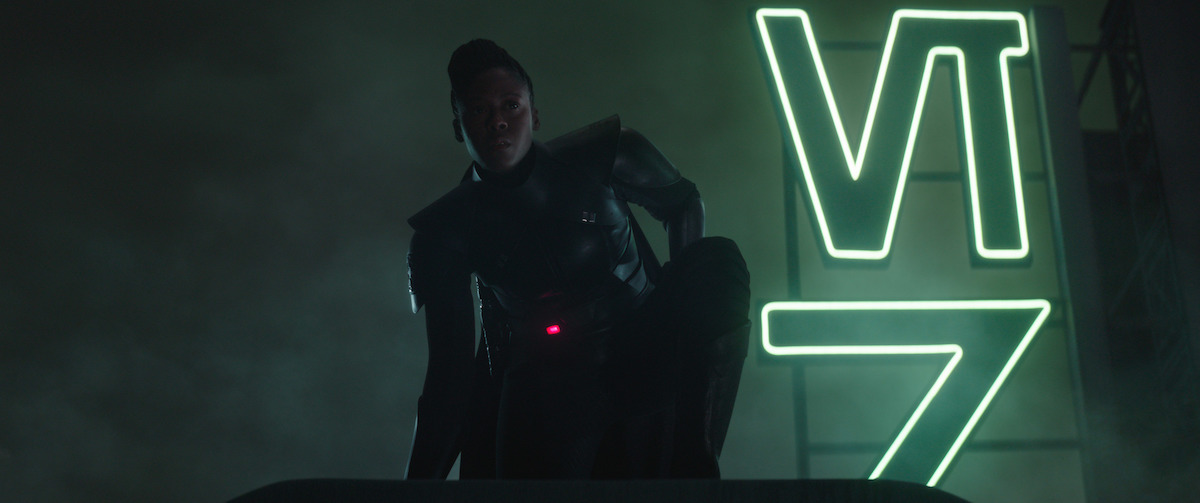 Reva kneeling near a neon sign on a rooftop on the planet Daiyu