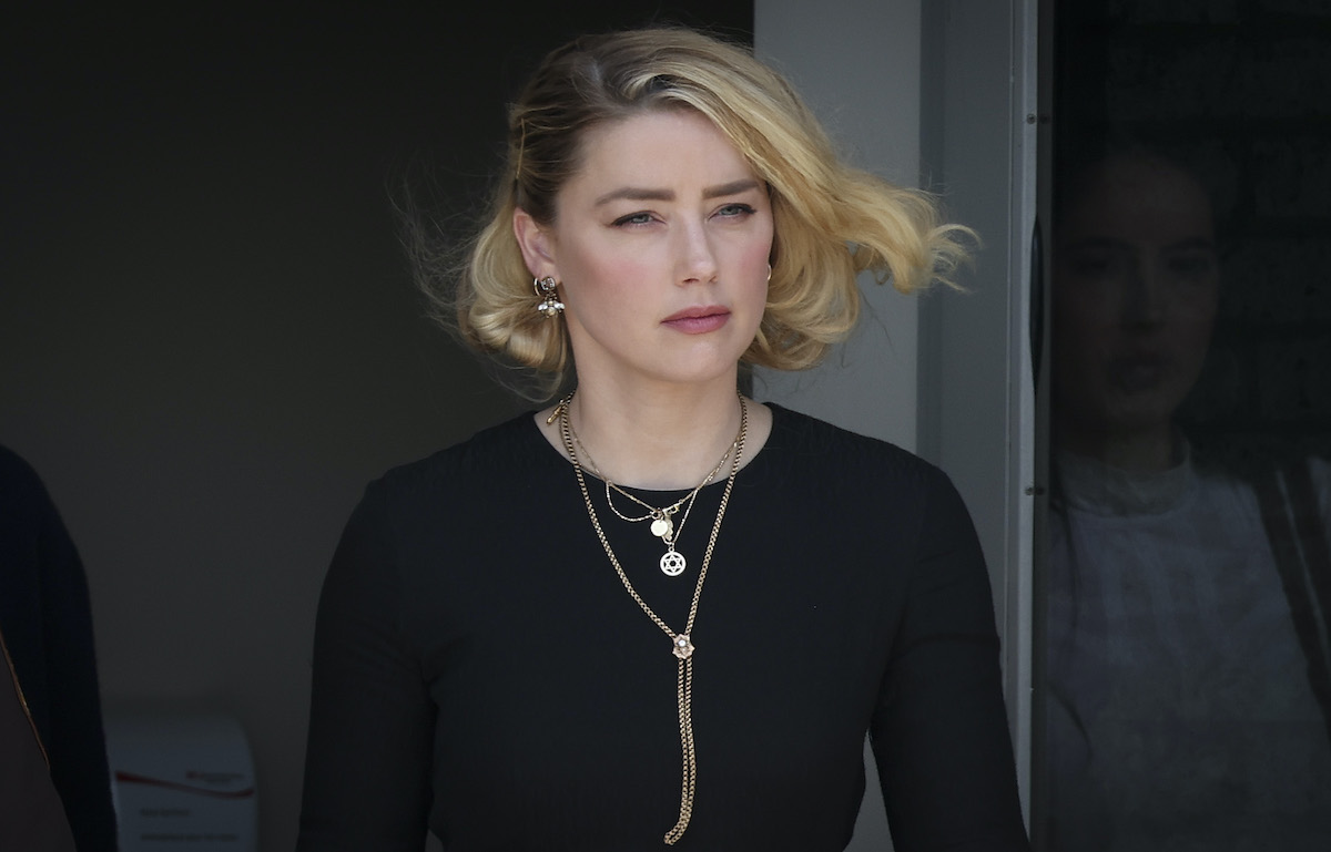 Amber Heard exits a building and the wind blows her hair, wearing a black shirt and multiple necklaces.