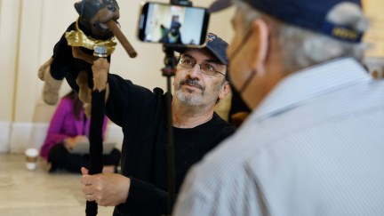 Actor and comedian Robert Smigel performs as Triumph the Insult Comic Dog in a hallway, being filmed by a cameraman