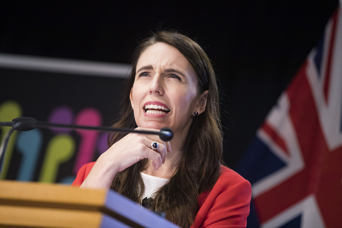 New Zealand Prime Minister Jacinda Ardern speaks at a podium, placing her hand on her chin