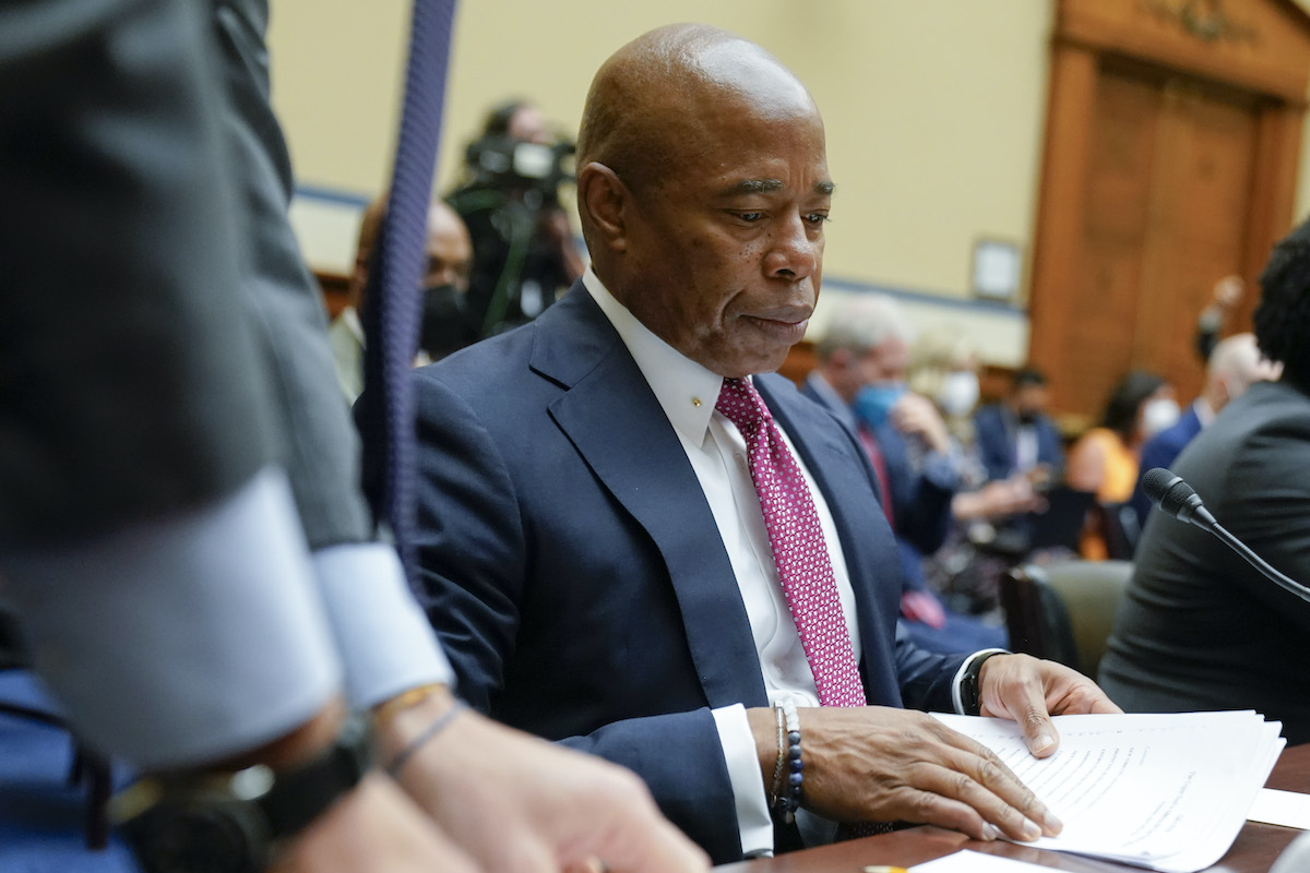 Eric Adams looks through a stack of papers, sitting at a desk during a congressional hearing