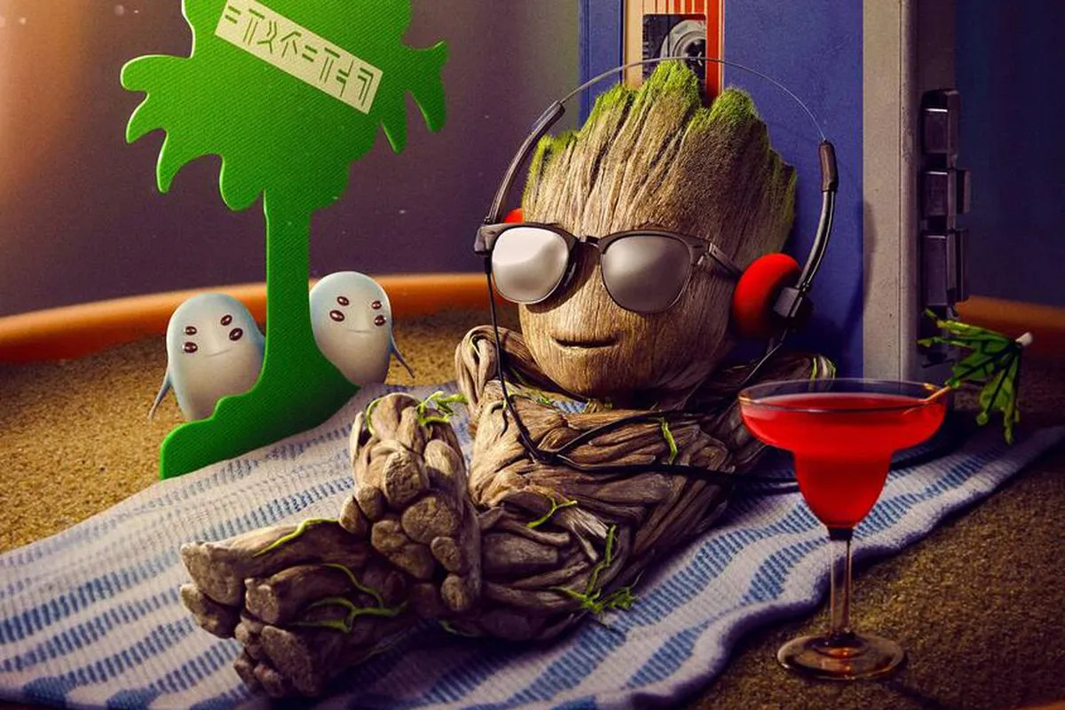 Baby Groot in sunglasses, sitting on a beach towel next to a palm tree air freshener.