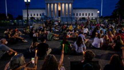 Portesters sit outside the Supreme Court at night during a candlelight vigil