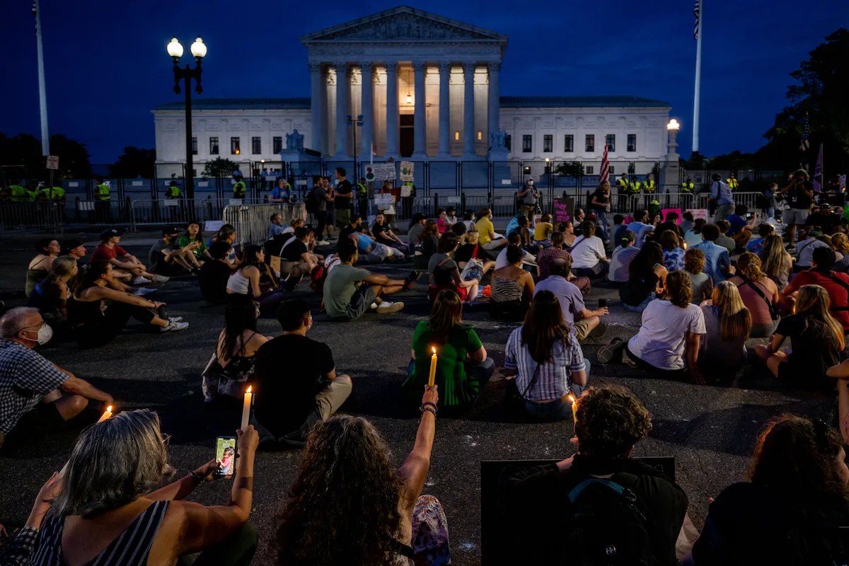 Portesters sit outside the Supreme Court at night during a candlelight vigil