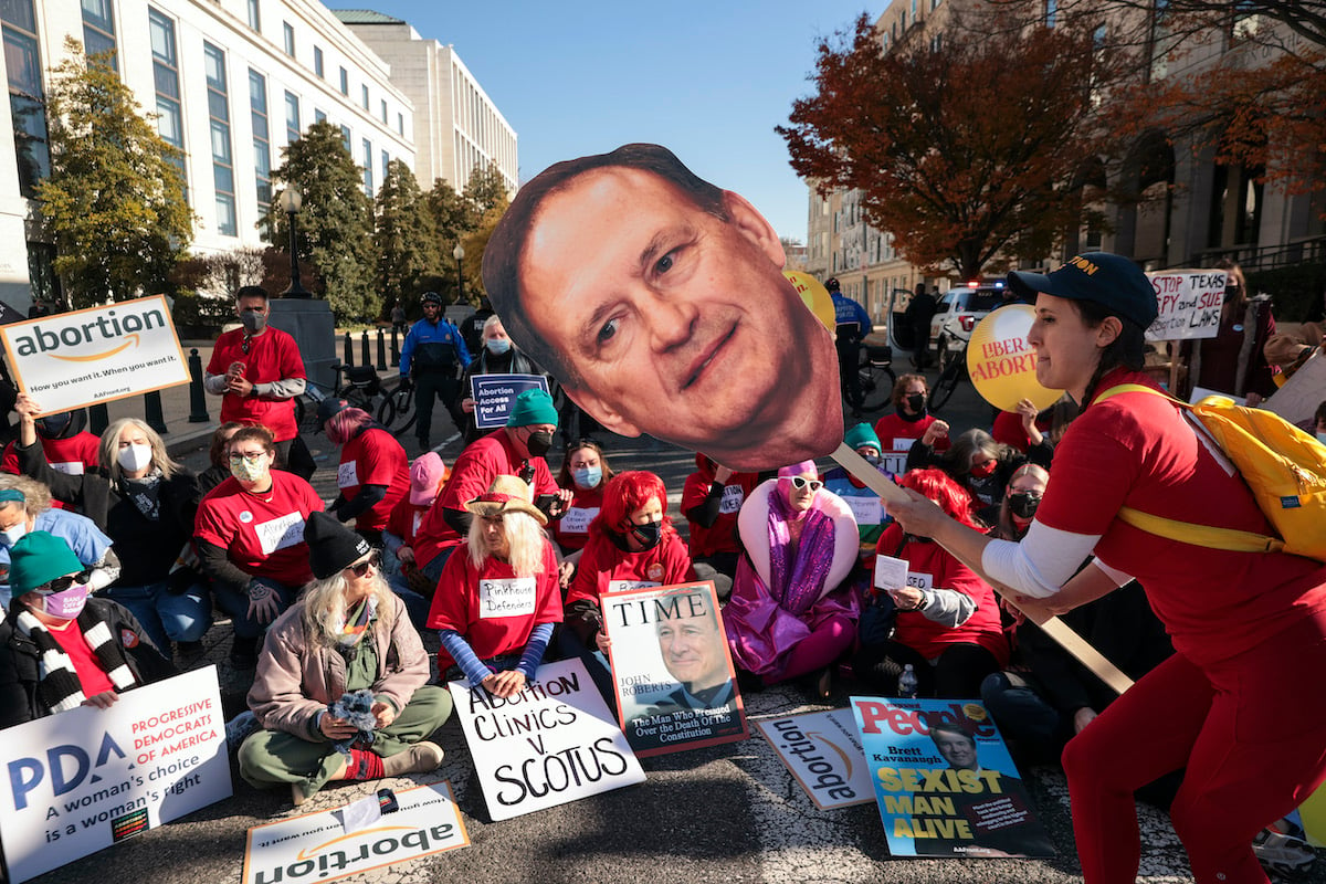 A group of abortion rights protesters, with one holding a giant photo cutout of the face of Samuel Alito