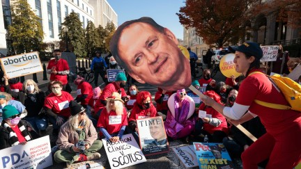 A group of abortion rights protesters, with one holding a giant photo cutout of the face of Samuel Alito