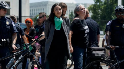 Alexandria Ocasio-Cortez walks with her hands behind her back, flanked by police after a protest
