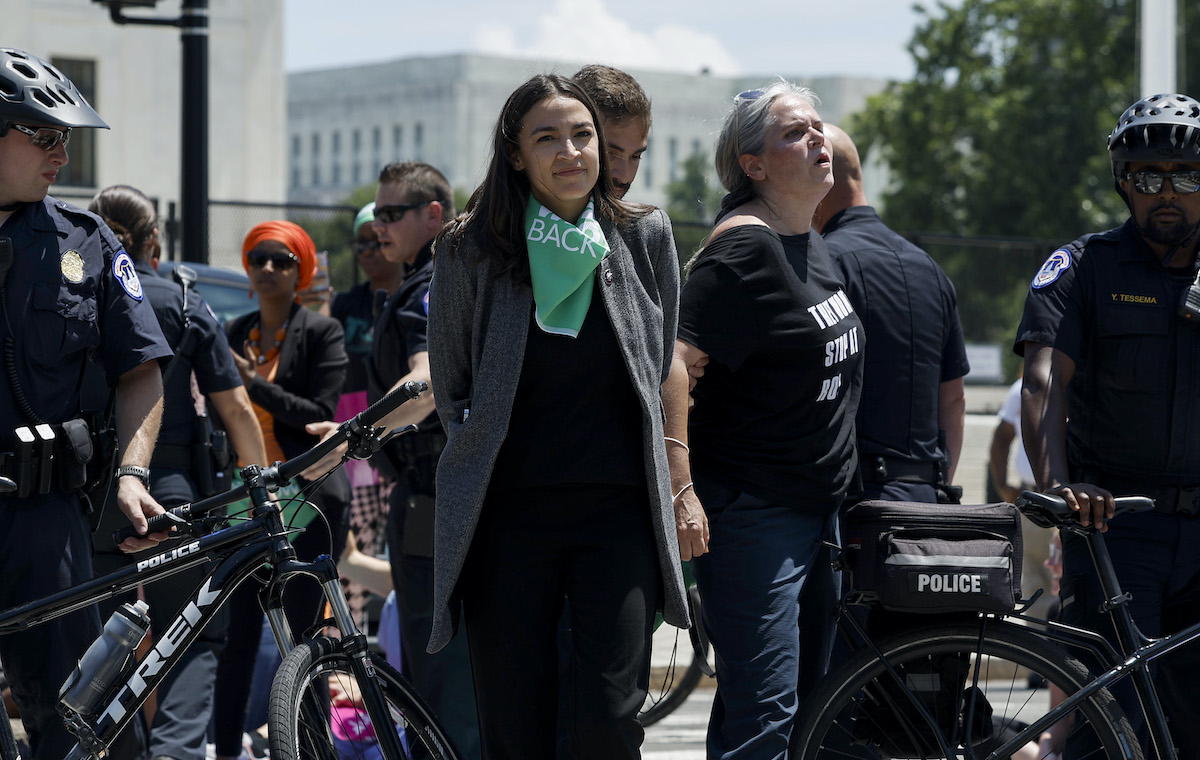 Alexandria Ocasio-Cortez walks with her hands behind her back, flanked by police after a protest
