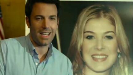 Nick Dunne (Ben Affleck) smiles awkwardly in front of a large missing poster of his wife Amy