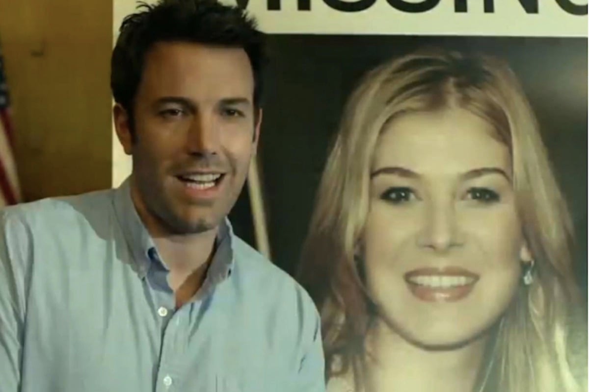Nick Dunne (Ben Affleck) smiles awkwardly in front of a large missing poster of his wife Amy
