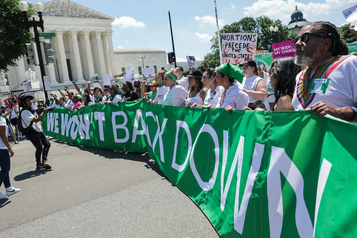 Abortion rights activists protest outside the U.S. Supreme Court, holding a huge green banner reading "we won't back down"