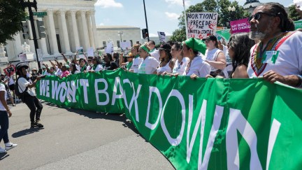 Abortion rights activists protest outside the U.S. Supreme Court, holding a huge green banner reading 
