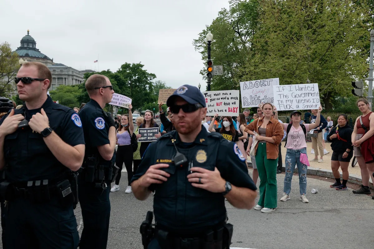 U.S. Capitol police officers stand in front of abortion rights demonstrators outdoors on a public street.