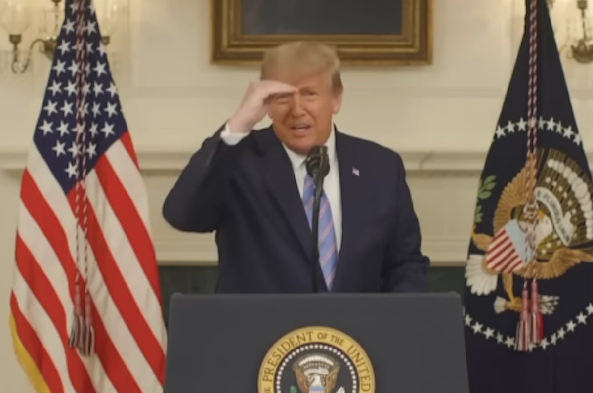 Donald Trump squints with his hand shielding his face while reading from a teleprompter from a podium