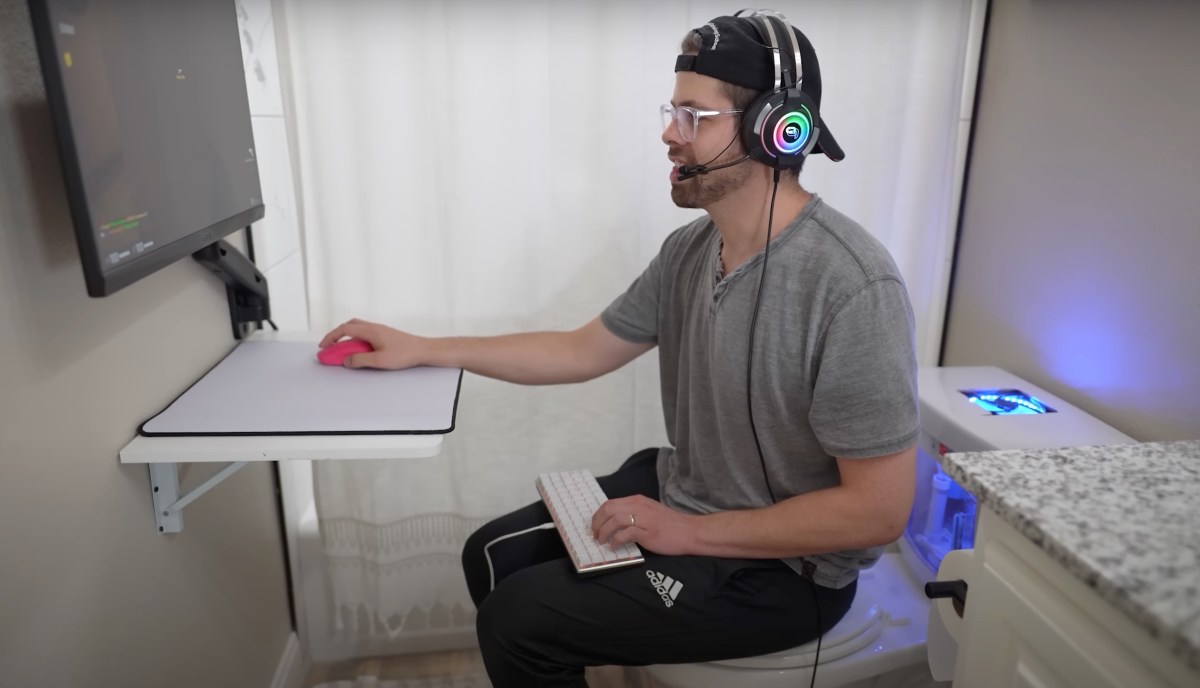YouTuber Basically Homeless sits on his toilet, which has a PC in the tank, and plays PC games.