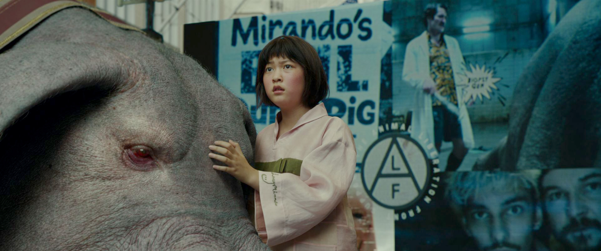 Film still from Okja featuring Ahn Seo-hyun as Mija, who is looking concerned as she rests her hand on Ojka's head
