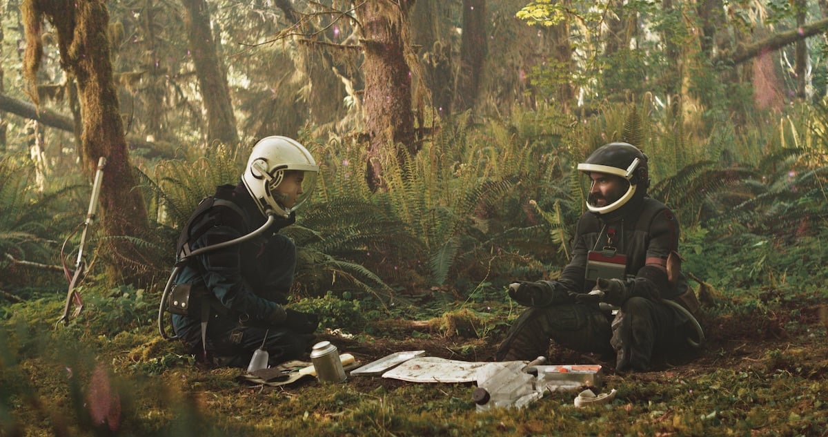 Film still from Prospect featuring Sophie Thatcher Cee and Jay Duplass as Damon crouching on the ground in a forest