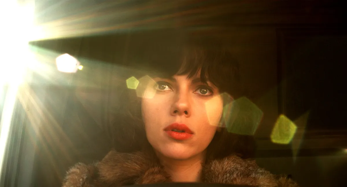 Film still from Under the Skin featuring Scarlett Johansson looking out the front windshield of a van with lens flare in the foreground