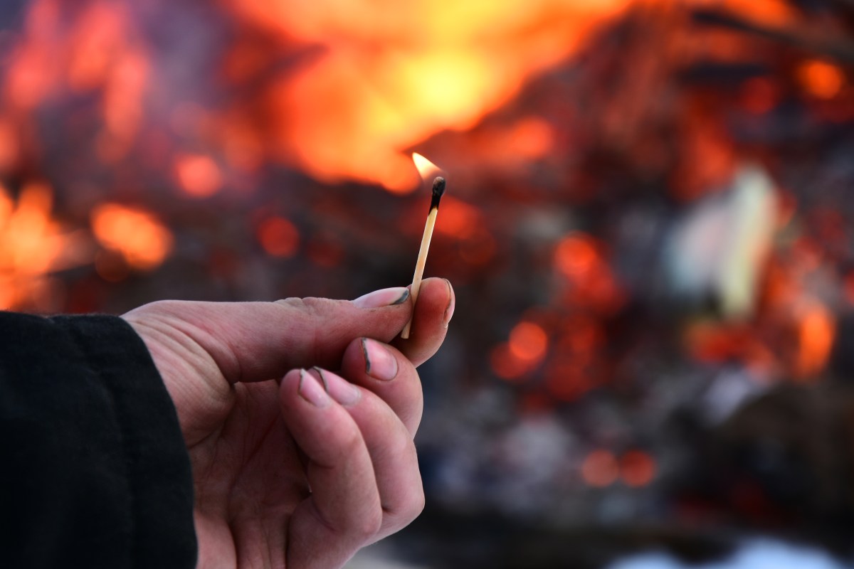 Man holds lit match in front of fire