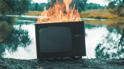 Retro vintage TV is on fire next to a pond.