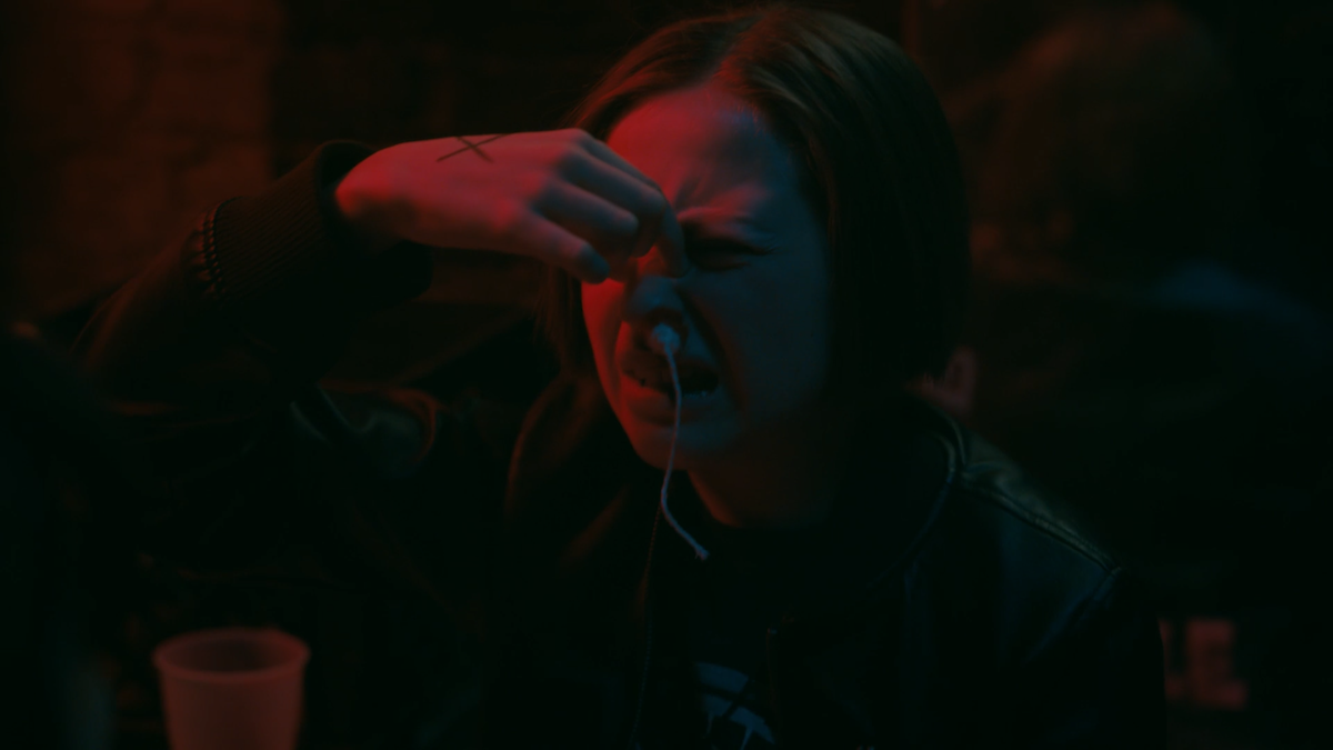 Mac, played by Sofia Rosinsky, squeezing the bridge of her bleeding nose, with a tampon shoved up one nostrilMac, played by Sofia Rosinsky, squeezing the bridge of her bleeding nose, with a tampon shoved up one nostril