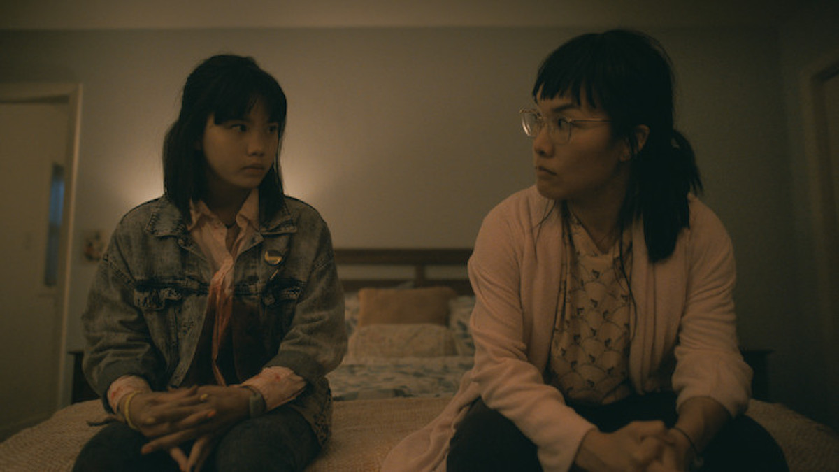 Erin, played by both Riley Lai Nelet and Ali Wong, sitting on the edge of a bed looking at each other