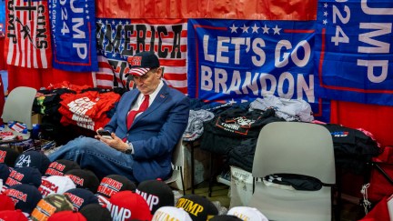 An older white man sits among rows of MAGA merchandise at CPAC.